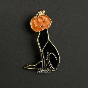 May include: Black enamel pin of a dog wearing a pumpkin on its head. The pumpkin is orange with a black stem and a carved face. The dog is sitting with its tail curled around its legs. The pin is on a black background.