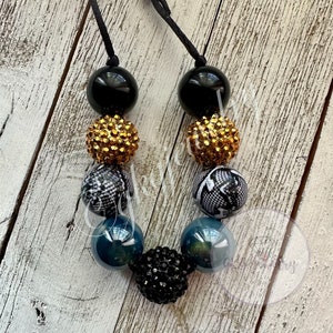 May include: A black and gold beaded necklace with black and white patterned beads, teal blue beads, and black rhinestone beads.