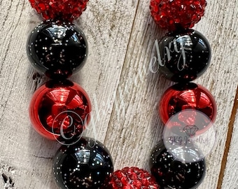 May include: A necklace featuring alternating red and black beads. The red beads have a textured, crystal-like appearance, while the black beads are glossy with silver glitter. The necklace is strung on a black cord. The necklace is a piece of jewelry.