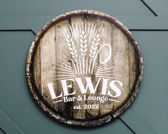 May include: A round wooden sign with a brown wood grain pattern. The sign has a white wheat stalk design and the text "LEWIS Bar & Lounge est. 2022" in white.