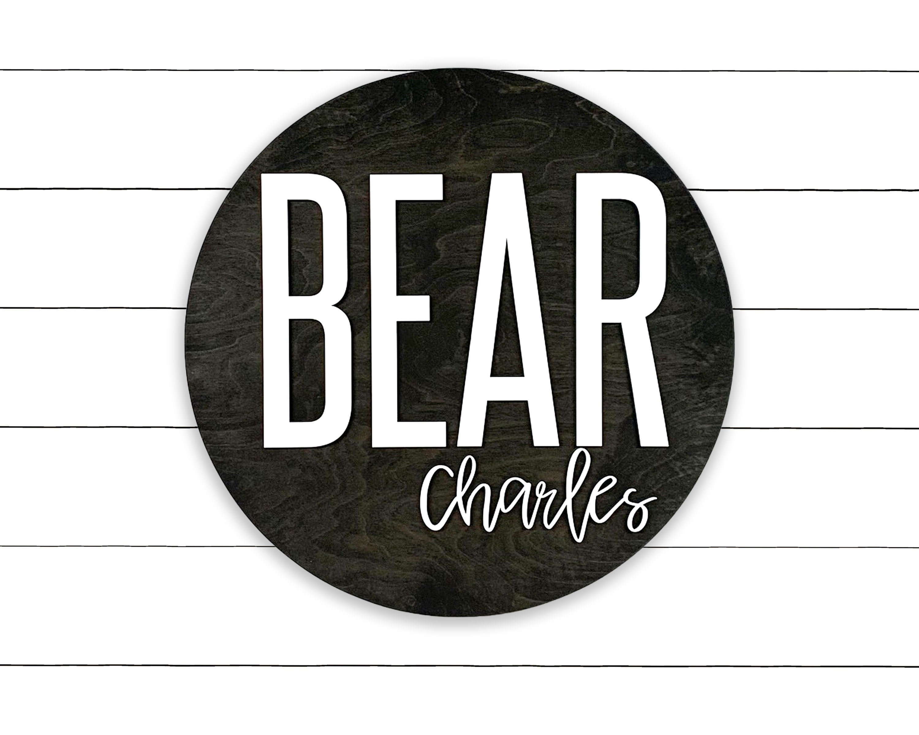 May include: A round wooden sign with the word "BEAR" in white letters and the name "charles" written in cursive underneath.