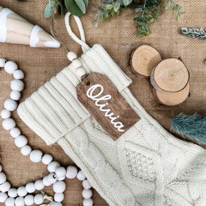 May include: White knitted Christmas stocking with a wooden tag that says "Olivia".