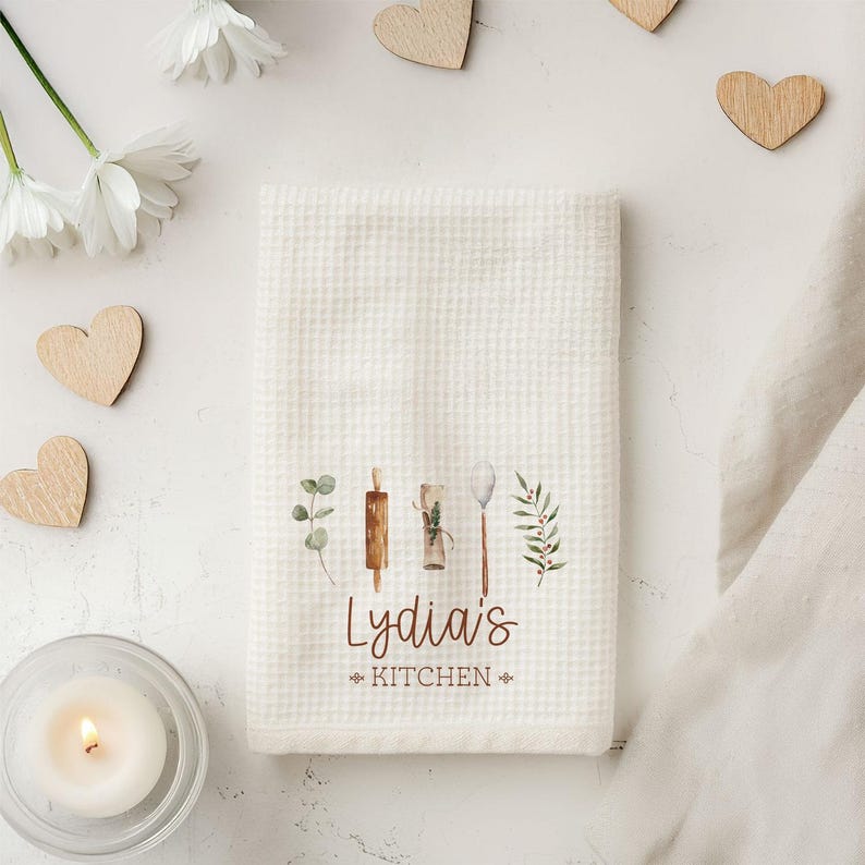May include: White kitchen towel with a brown and green watercolor design of kitchen tools and the text "Lydia's Kitchen".