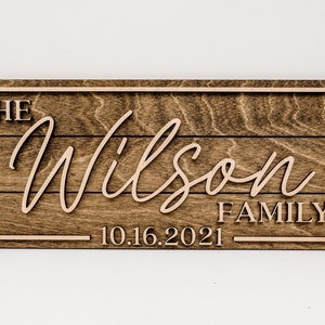 May include: A wooden sign with the text "The Wilson Family 10.16.2021" in a light brown color. The sign has a rustic wood grain texture and a dark brown frame.