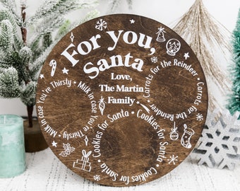 May include: A round wooden sign with white text that reads "For you, Santa" and includes a list of items for Santa, such as milk, cookies, and carrots for the reindeer. The sign is decorated with stars and other festive designs.