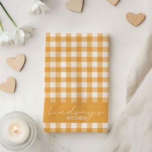 K&ouml;nnte beinhalten: Ein gelbes und wei&szlig;es kariertes Geschirrtuch mit dem Text "Lindsay's Kitchen" auf der Unterseite.
