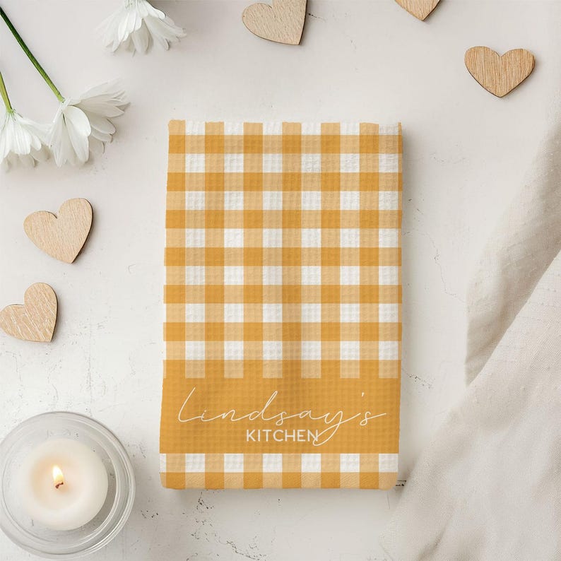 K&ouml;nnte beinhalten: Ein gelbes und wei&szlig;es kariertes Geschirrtuch mit dem Text "Lindsay's Kitchen" auf der Unterseite.