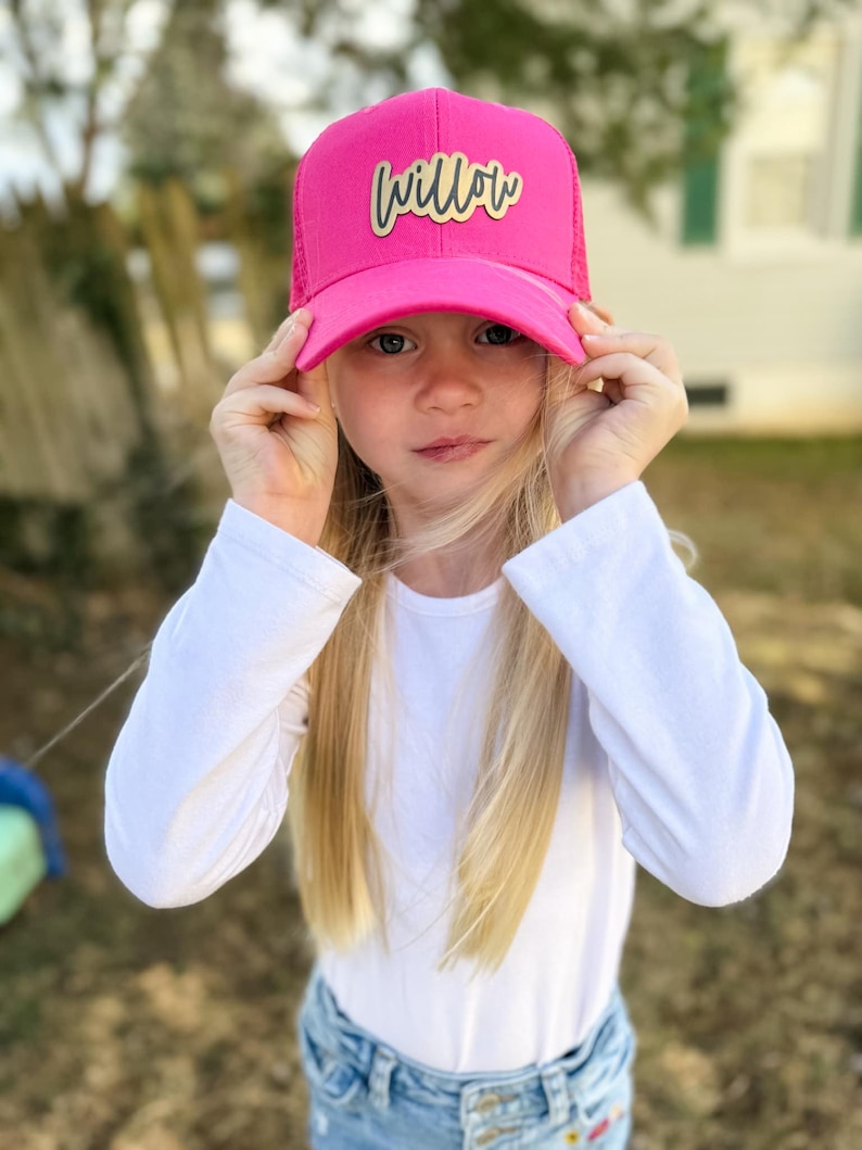 May include: A pink trucker hat with a gold mesh back and a gold "Willow" patch on the front.