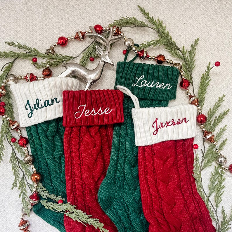May include: Four red and green knitted Christmas stockings with white cuffs. The stockings are decorated with the names "Julian", "Jesse", "Lauren", and "Jaxson" in green embroidery.