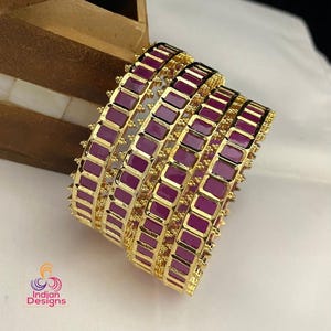May include: Set of four gold bangles with purple enamel and square designs. The bangles are stacked on top of each other.