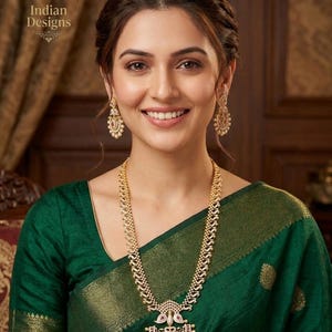 May include: A woman wearing a gold necklace and earrings with a green dress. The necklace has a large pendant with a red stone. The earrings are pearl-like. The text "Indian Designs" is in the upper left corner.