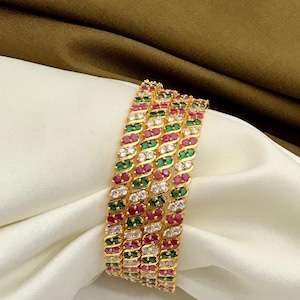 May include: Set of four gold bangles with white, green, and pink stones. The bangles are stacked on top of each other.