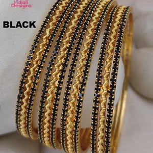 May include: Gold-toned bangles with black accents. The bangles feature a repeating pattern of black stones and a textured gold design. The word "BLACK" is printed in bold, black letters.