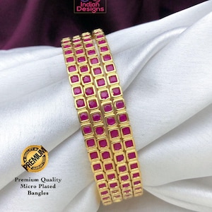 May include: Set of four gold bangles with pink square stones. The bangles are stacked on top of each other. The text "Premium Quality Micro Plated Bangles" is visible below the image.
