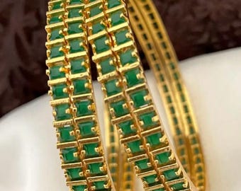 May include: Two gold bangles with green square-shaped stones set in a repeating pattern.