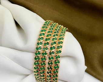May include: Set of four gold bangles with green gemstone accents. The bangles are stacked on top of each other.