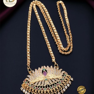 May include: Gold-colored micro-plated chain pendant with a lotus flower design. The pendant is adorned with clear and colored gemstones. The chain has a textured, linked pattern. The image also includes the text "Premium Quality Micro Plated Chain Pendant."