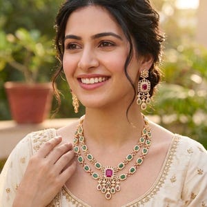May include: A two-layered gold necklace featuring rectangular green stones and a central rectangular pink stone with dangling accents, paired with matching drop earrings that feature a pink stone top and a green stone bottom dangle.