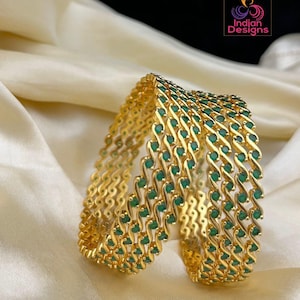 May include: A set of six gold bangles with green stones. The bangles are stacked on top of each other and have a wavy design.