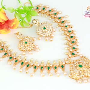May include: A gold necklace and earrings set with white stones and green accents. The necklace features a pendant with a floral design and a row of teardrop-shaped stones. The earrings are similar in design to the pendant.