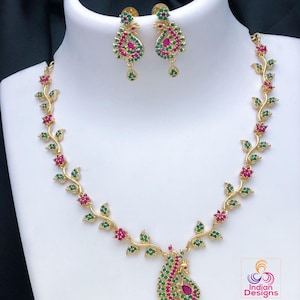 May include: Gold necklace with a peacock pendant and matching earrings. The necklace features a vine design with green and pink stones.