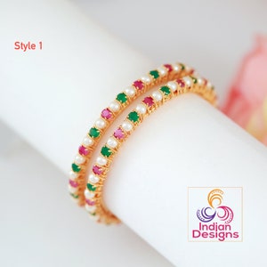 May include: Two gold bangles with alternating pink, green, and white stones. The bangles are stacked on top of each other.