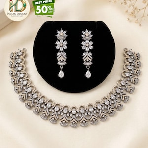 May include: A white ceramic mug with a black handle and the text "But First, Coffee" in a bold, black font. The mug is set against a blurred background, suggesting a cozy setting.