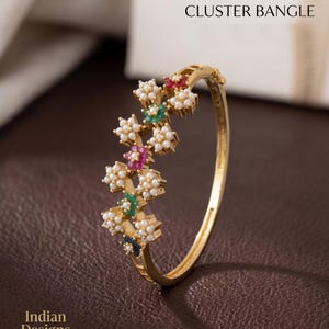 May include: Gold-toned bangle with a floral cluster design. The clusters feature small white pearls and colorful gemstones in red, green, and blue. The text on the image reads "MULTICOLOR FLORAL CLUSTER BANGLE."