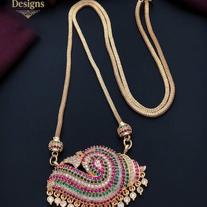May include: A gold-toned necklace featuring a textured chain and a large, curved pendant adorned with rows of small, vibrant pink, green, and clear stones. The pendant has a dangling fringe of small, clear circular stones along the bottom edge.