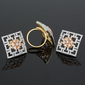 May include: A set of gold-tone jewelry featuring a square design with clear and pink stones. The set includes a ring and a pair of earrings.