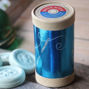 May include: A blue and white tin container with the text "Button, Button" and "For Special Occasions Fragranced Guest Soaps" printed on the lid. The tin contains small, round, light blue soaps shaped like buttons.