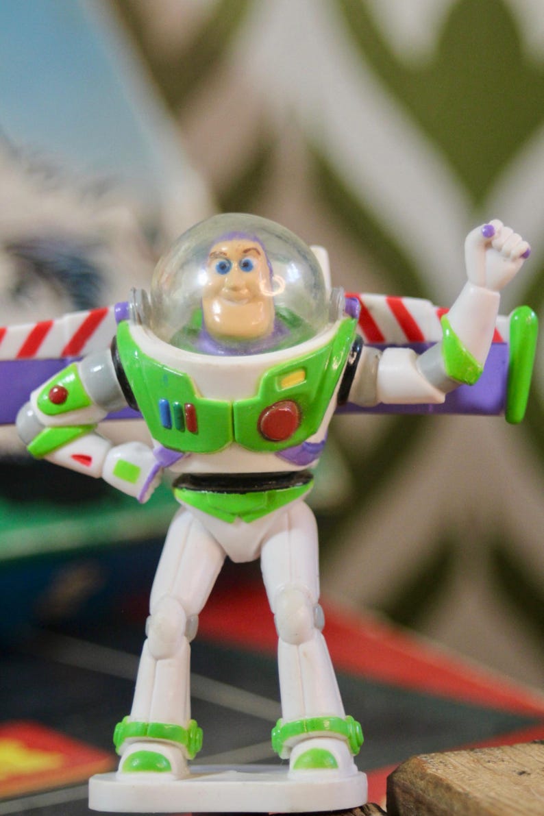 Puede incluir: Figura de acci&oacute;n de Buzz Lightyear, con casco transparente, traje espacial verde y blanco, y alas moradas. La figura est&aacute; posando con un brazo levantado, un dise&ntilde;o ic&oacute;nico de la franquicia Toy Story.