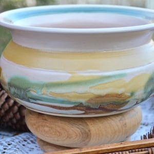 May include: A ceramic planter with a light brown, yellow, and blue glaze. The planter is sitting on a wooden stand.