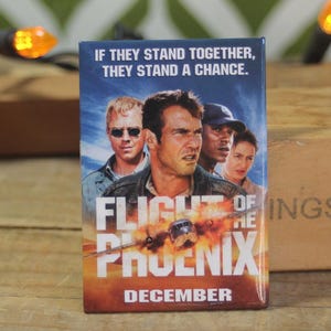 May include: A movie poster for the film "Flight of the Phoenix" with the tagline "If they stand together, they stand a chance." The poster features a group of men in front of a burning plane. The poster is set against a blue sky with clouds. The text "December" is at the bottom of the poster.