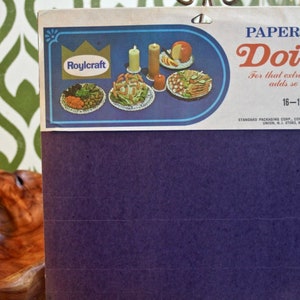 May include: A package of 16-inch paper doilies from Roylcraft. The package features a blue and white design with a crown logo and images of food on doilies. The text on the package reads "Paper Doilies" and "For that extra touch that adds so much."