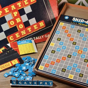 May include: A vintage Skip-A-Cross word tally game with a game board, letter tiles, and instruction cards. The game board is gray with colored squares. The game's name is printed in blue and white. The game is on a wooden surface.