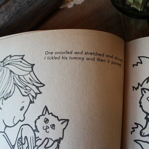 May include: A black and white illustration of a boy holding a kitten. The text reads: "One uncurled and stretched and stirred I tickled his tummy and then it purred."