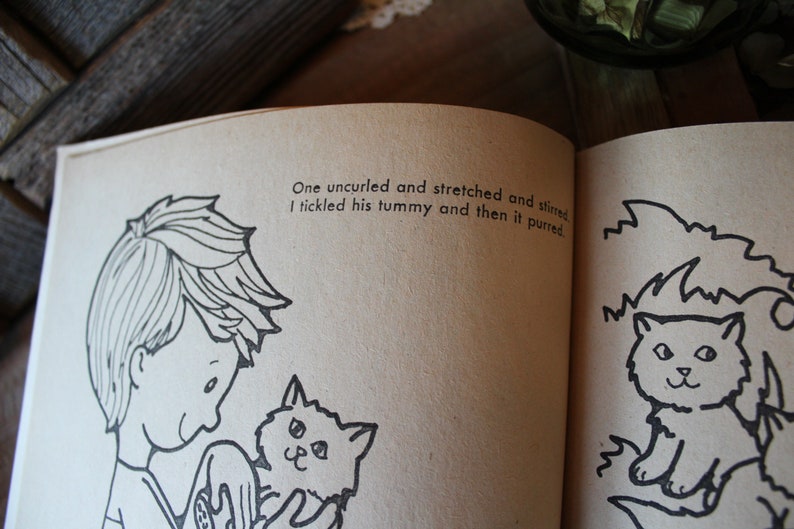 May include: A black and white illustration of a boy holding a kitten. The text reads: "One uncurled and stretched and stirred I tickled his tummy and then it purred."