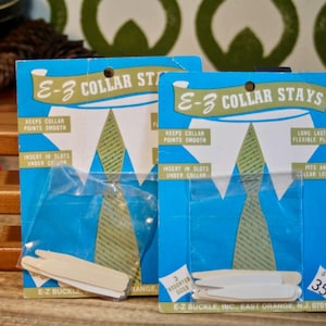 May include: Two packages of E-Z Collar Stays, a product that keeps collar points smooth. The packages are blue and white with a picture of a shirt collar. The text on the package reads "E-Z Collar Stays" and "Keeps Collar Points Smooth". The package also includes instructions on how to use the collar stays. The price is 35 cents for 6 collar stays.
