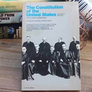 May include: A paperback book titled The Constitution of the United States with Case Summaries, edited by Edward Conrad Smith. The cover is light gray with blue text and a black and white photograph of a group of men in judicial robes.
