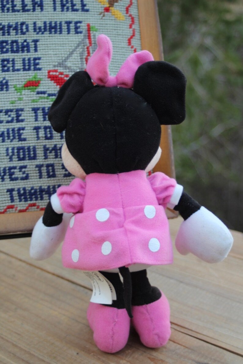May include: A pink and white polka dot dress with a black bow on top of the head. The plush toy is a black and white Minnie Mouse.