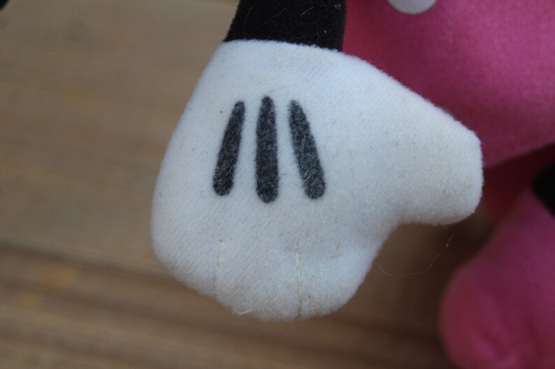 May include: Close-up of a white plush glove with three black stitched fingers. The glove is part of a plush toy.