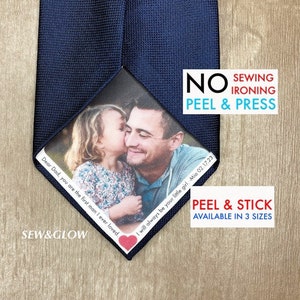 Peut inclure: Une cravate bleue avec une photo personnalisée d'un père et de sa fille. La photo est imprimée sur un carré blanc avec le texte "Cher papa, tu es le premier homme que j'ai jamais aimé." et "Je serai toujours ta petite fille. Mia 02.17.23". Le texte "NO SEWING IRONING PEEL & PRESS" est imprimé en rouge et noir sur la cravate. Le texte "PEEL & STICK AVAILABLE IN 3 SIZES" est imprimé en bleu et blanc sur la cravate.