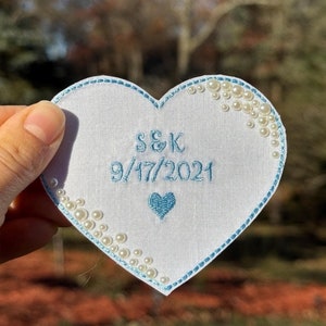 May include: White heart-shaped fabric patch with blue embroidery. The patch features the initials "S&K" and the date "9/17/2021". The edges of the patch are decorated with white pearl-like beads.