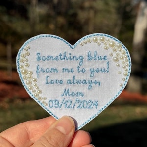 May include: White heart-shaped fabric patch with blue embroidery that reads "Something blue from me to you! Love always, Mom 09/12/2024". The patch is decorated with white pearl-like beads around the edge.