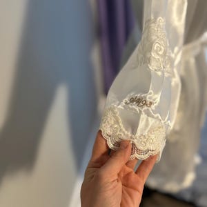 May include: White satin robe with a lace trim and embroidered detail. The embroidery reads 'glaze'. 