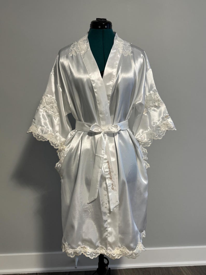 May include: A white satin robe with lace trim and a satin sash. The sash has the words 'Happy Mother's Day' embroidered on it.