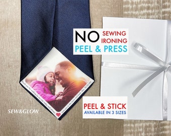 May include: A blue tie with a photo of a father and daughter printed on it. The photo is in a heart-shaped frame. The text "Sew & Glow" is printed on the bottom left corner of the photo. The text "No Sewing, Ironing, Peel & Press" is printed on a white label. The text "Peel & Stick Available in 3 Sizes" is printed on a white label.