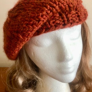 May include: A rust-coloured knitted beret with a textured pattern.