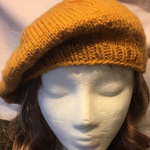 May include: A mustard yellow knitted beret. The beret is made of a soft, textured yarn and has a simple, classic design.